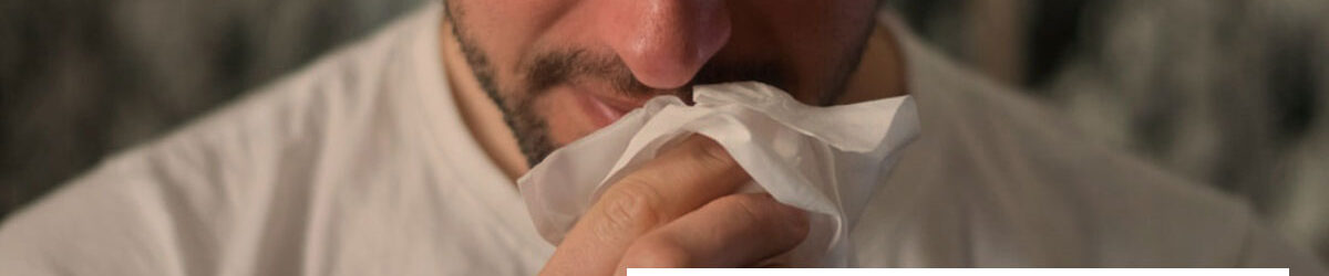 Man with a beard bowing forward and wiping his runny nose with a tissue. Our title is below him: VA Rating for Chronic Rhinitis
